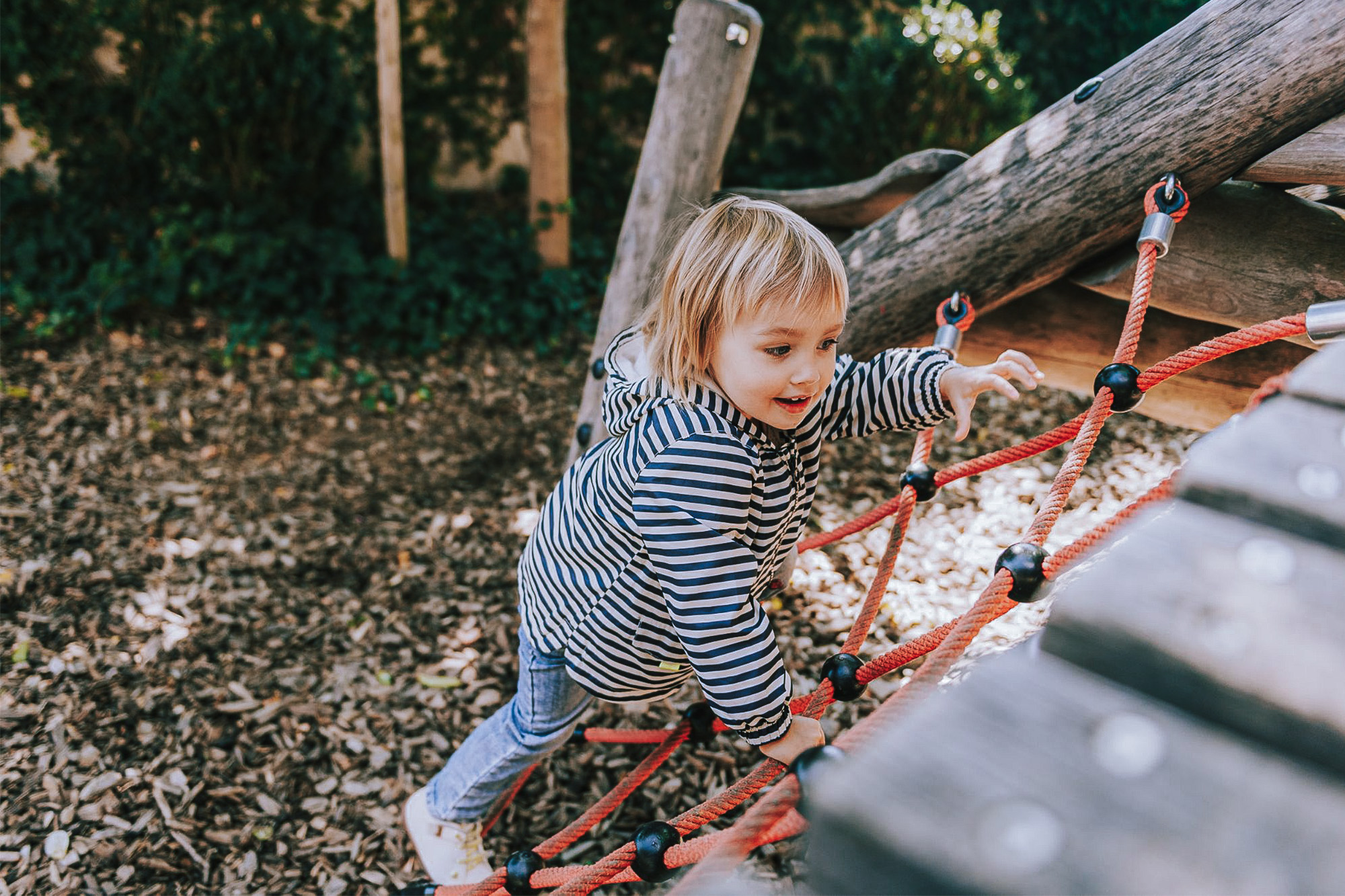 Kind klettert auf einem Spielplatz über ein Kletternetz